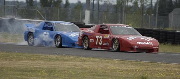 red #73 Nissan 240SX race car of Dave Humphrey just in front of blue #53 race car of Collin Jackson. Smoke comes from the tires of the blue race car