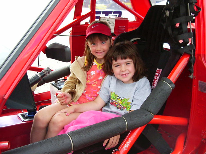 Two young girls smile while in the drivers seat of the red Datsun 510